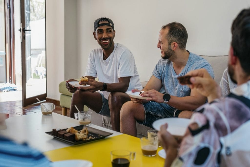 african american man smiles while eating pastries at a gathering of friends