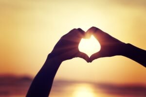 Hands making a heart shape on sunrise seaside