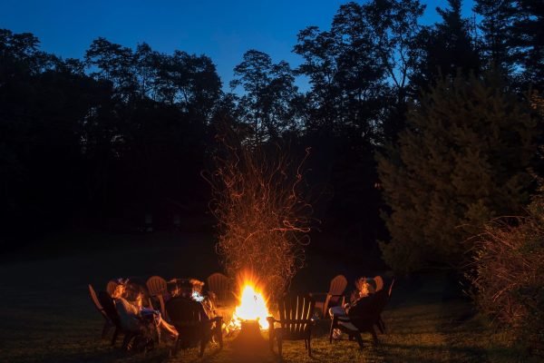 A group of people seated around a campfire at dusk.